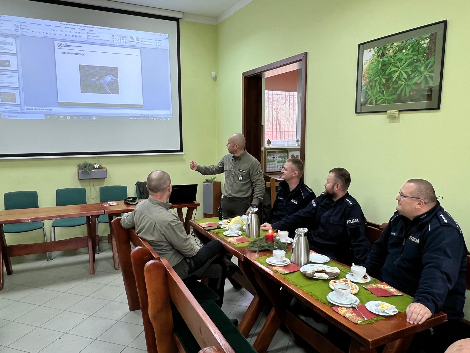 Zdjęcie przedstawia komendanta posterunku straży leśnej w Nadleśnictwie Piaski prowadzącego prezentację podsumowującą  oraz innych uczestników spotkania (fot. archiwum nadleśnctwa, C. Rosiak) 